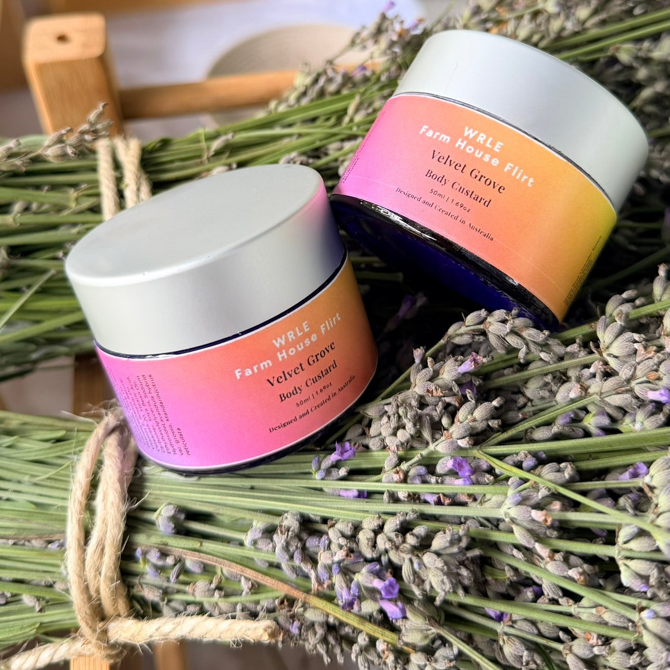 Two jars of body cream on a bed of lavender with a blurred outdoor background