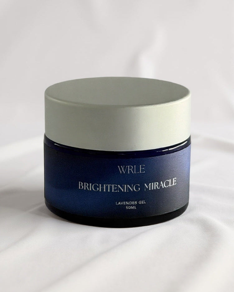 A beautiful blue glass jar labeled 'Brightening Miracle' by WRL on a white background